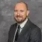 Professional headshot of a man with beard wearing a dark suit and tie.